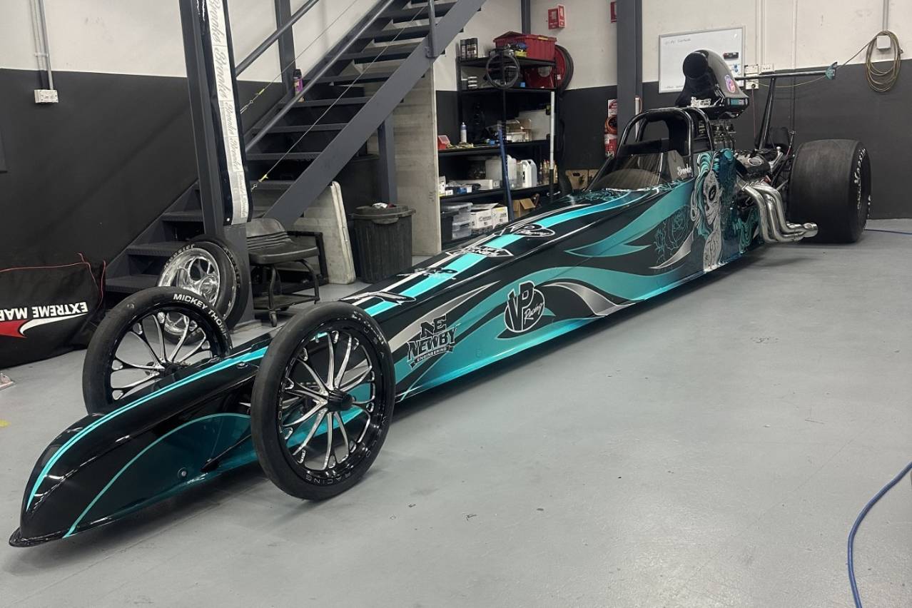 Brooke Rapisarda’s black and aqua Modified dragster parked inside a workshop.